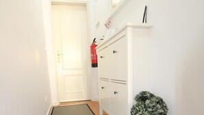 A narrow hallway with a grey mat, white walls, a wooden floor, a white door, and a white cabinet with a potted plant.