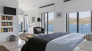 A modern bedroom with a large bed, a desk, and a chair. There is a bookshelf, a television, and a window with a view of the sea. - Beachfront Villa Poseidon with Heated Pool (Korcula)