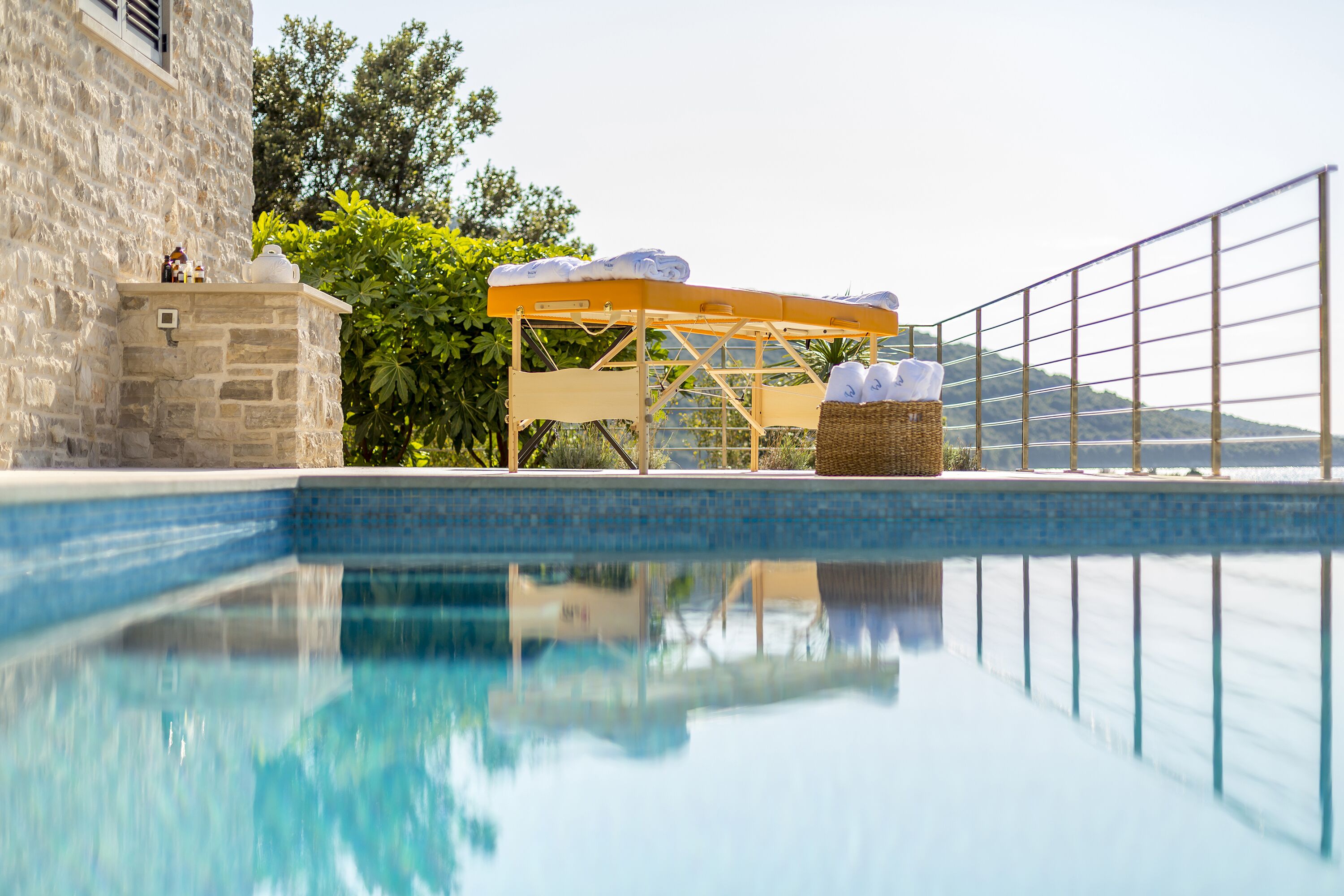 Ein Pool mit Sonnenschirm, einer Steinmauer und einem Korbwesen mit Flaschen.