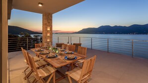 An outdoor dining area with a view of a lake and mountains at dusk. - Beachfront Villa Poseidon with Heated Pool (Korcula)