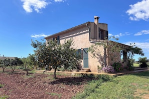A two-story building with a stone facade, a small garden, and a clear blue sky.