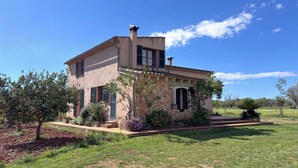 A two-story house with a stone facade, a tiled roof, and a well-maintained garden with various plants and a lawn. - Nice relaxing country house with private pool (Inca)