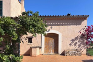 Un edificio con una puerta de madera grande, un banco de piedra y un árbol en primer plano.