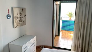 Ein Schlafzimmer mit einem Bett, einem Schminktisch, einem Gemälde und einer Glastür, die auf einen Balkon führt.