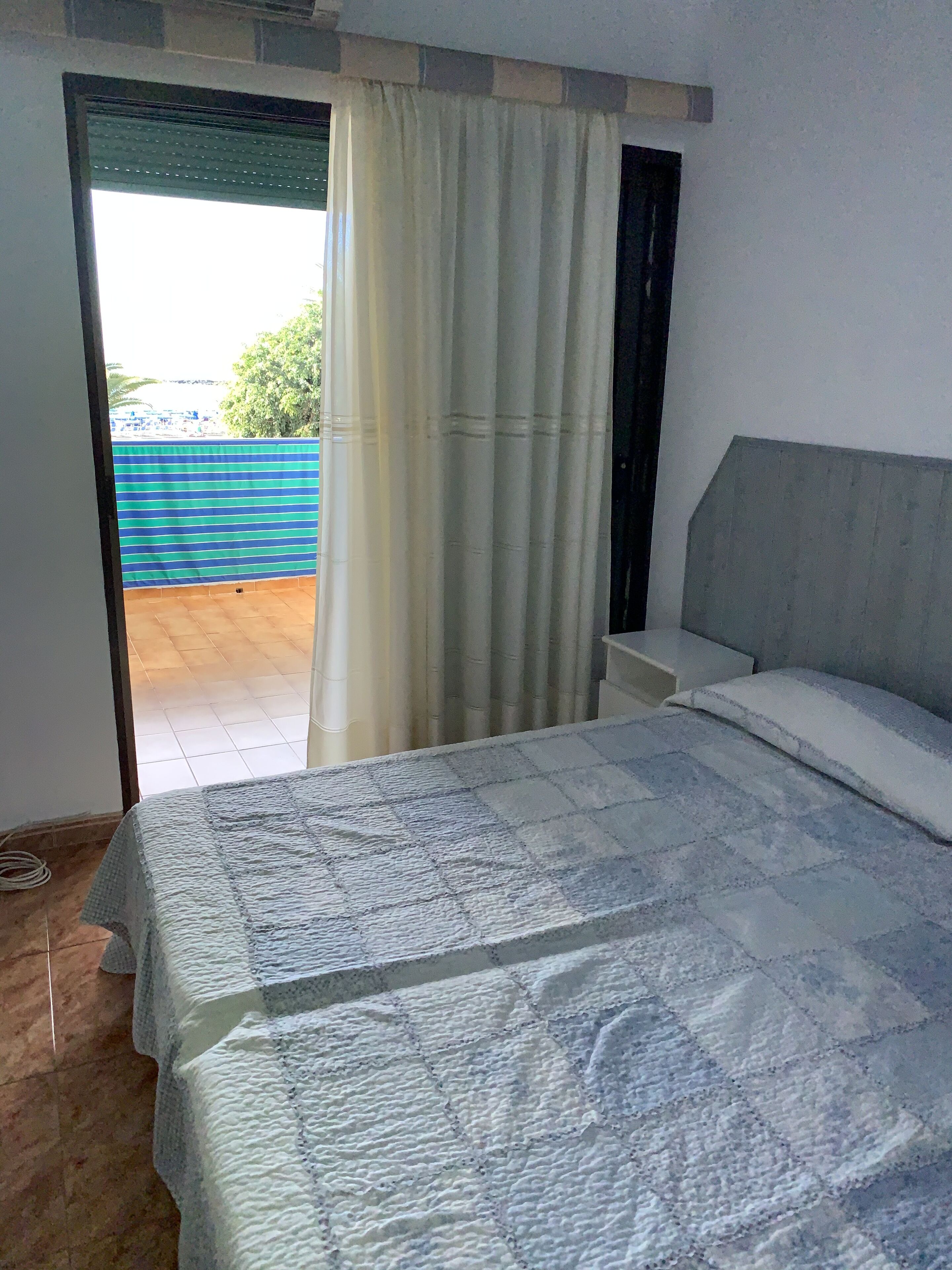 Un dormitorio con cama, ventana con cortinas y vistas a una cerca azul y follaje exterior.