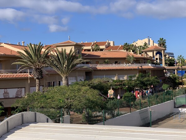 A residential building with multiple balconies, a palm tree, and a fenced area with a playground.