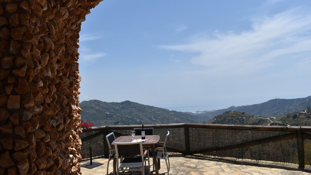 Un muro di pietra con tavolo e sedie su una terrazza che si affaccia su un paesaggio montuoso.