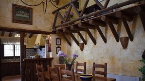 Un'accogliente zona pranzo con sedie e tavolo in legno, una trave in legno a soffitto e una pianta in vaso con fiori viola.
