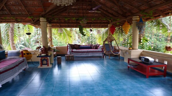 A spacious room with a blue tiled floor, a cushioned sofa, a hanging chair, and a small table with a speaker.