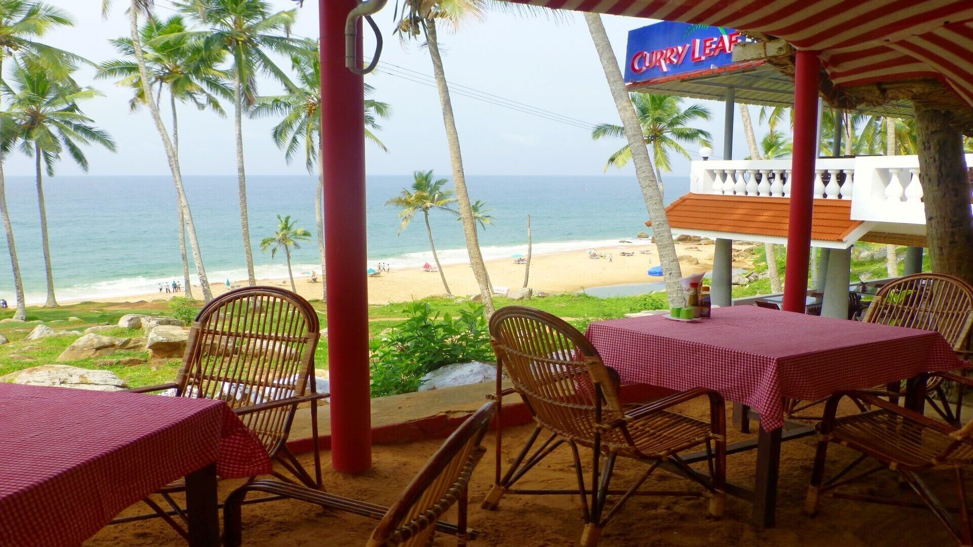 Un restaurant situé en bord de mer, avec des nappes à carreaux rouges et blancs, des chaises en osier et une vue sur l’océan et la plage.