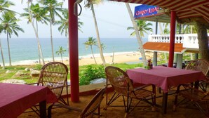 Un restaurant situé en bord de mer, avec des nappes à carreaux rouges et blancs, des chaises en osier et une vue sur l’océan et la plage.