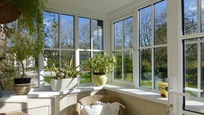 A sunroom with large windows, wicker furniture, and potted plants. - Family friendly cottage close to Praa Sands beach (Helston)