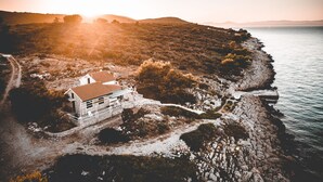 Vista aérea de una casa costera con un camino de piedra que conduce a la entrada, rodeada de terreno rocoso y vistas al mar.