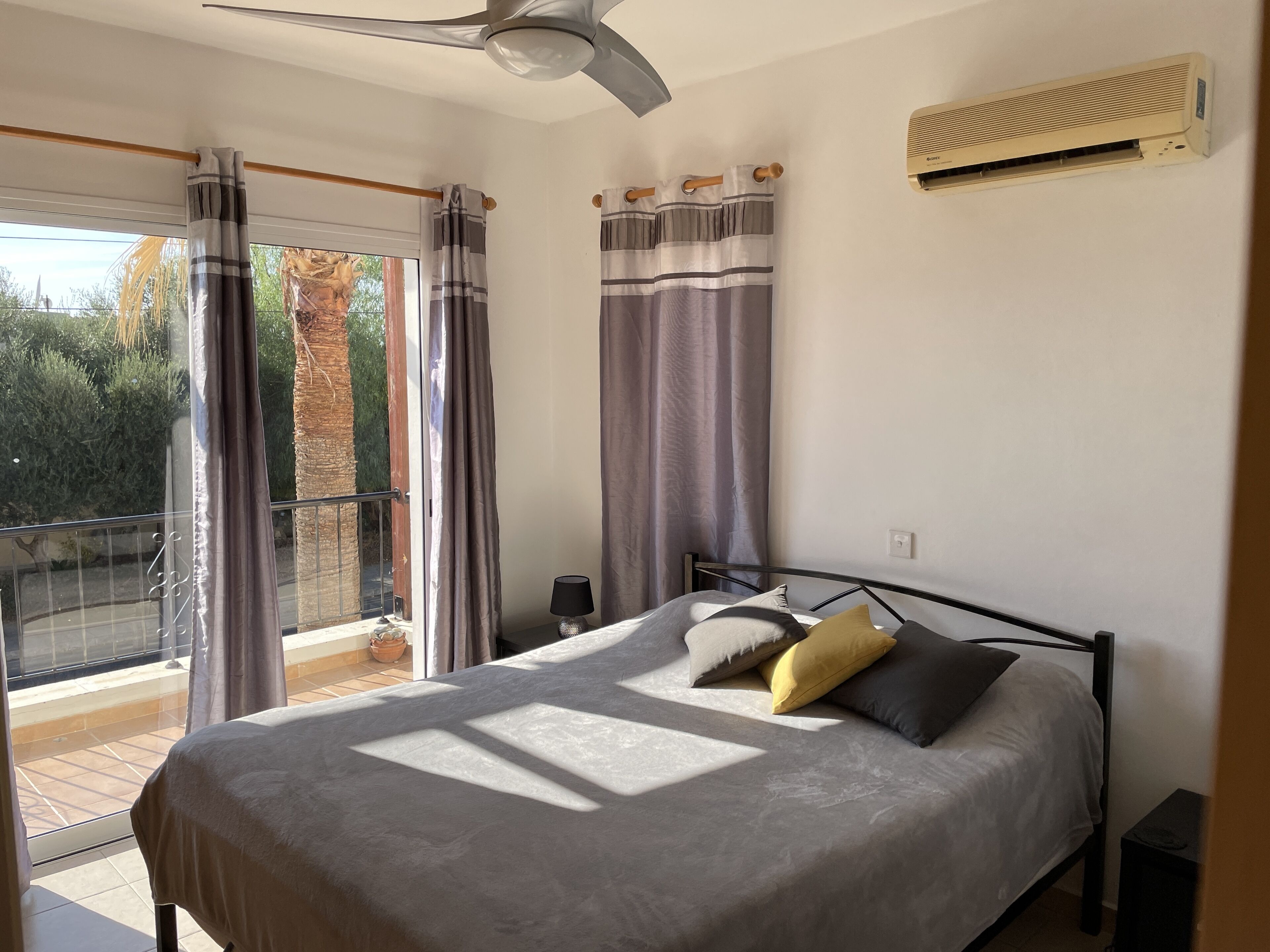 Une chambre à coucher avec un lit, des rideaux, un ventilateur de plafond, un climatiseur et une vue sur l’extérieur.