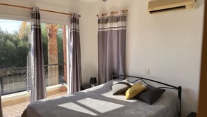 Une chambre à coucher avec un lit, des rideaux, un ventilateur de plafond, un climatiseur et une vue sur l’extérieur.