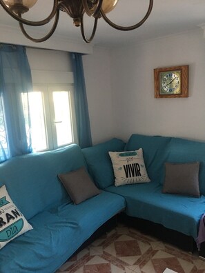 A living room with a blue sofa, a wall clock, and a window with curtains.