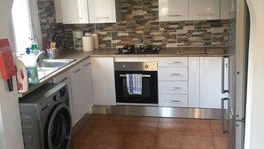 Una cuina compacta amb armaris blancs, una alsada de pedra, forn integrat i rentadora.