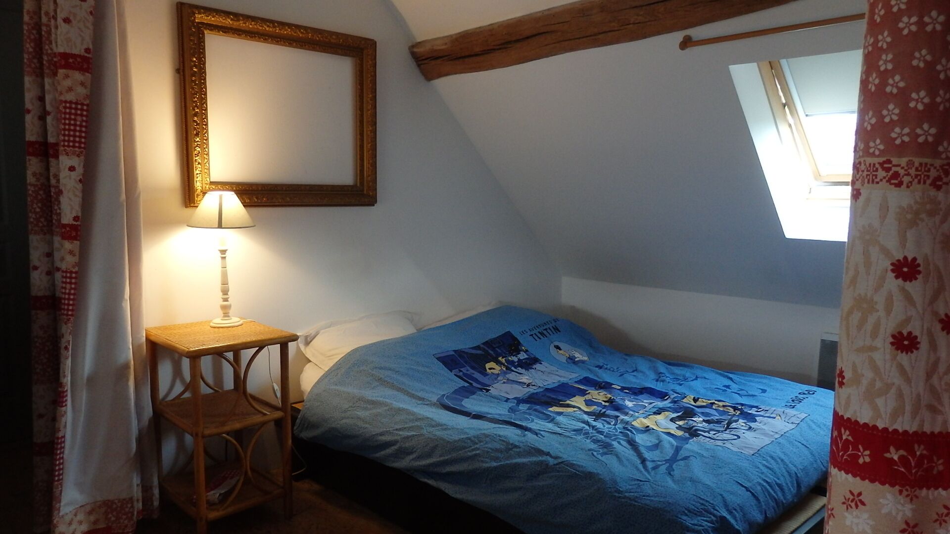 A bedroom with a single bed, a bedside table with a lamp, a wooden headboard, and a window with curtains.