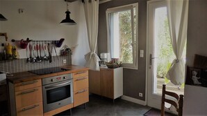 A kitchen with wooden cabinets, a built-in oven, and a window with curtains. - In the heart of the Chateaux of the Loire (Saint-Georges-sur-Cher)