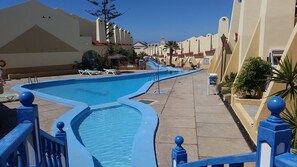 A swimming pool with a blue border, lounge chairs, and a tiled walkway. - Costa Adeje ground floor 1 bedroom sea & mountain view apartment (Costa Adeje)
