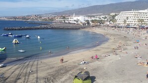 Una playa con un rompeolas rocoso, un hotel grande al fondo y gente tomando el sol.