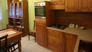 A kitchen with wooden cabinets, a stove, and a dining area with a table and chairs. - MAISON CASSIUS LO VERT (ISSOGNE  ITALIA)