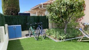 Un jardin bien entretenu avec une pelouse artificielle, deux vélos, une armoire bleue et un arbre.