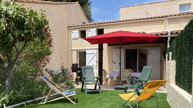 Une terrasse avec du gazon synthétique, du mobilier d’extérieur et un parasol rouge.