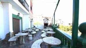A courtyard with stone tables and chairs, a green railing, and a building entrance in the background.
