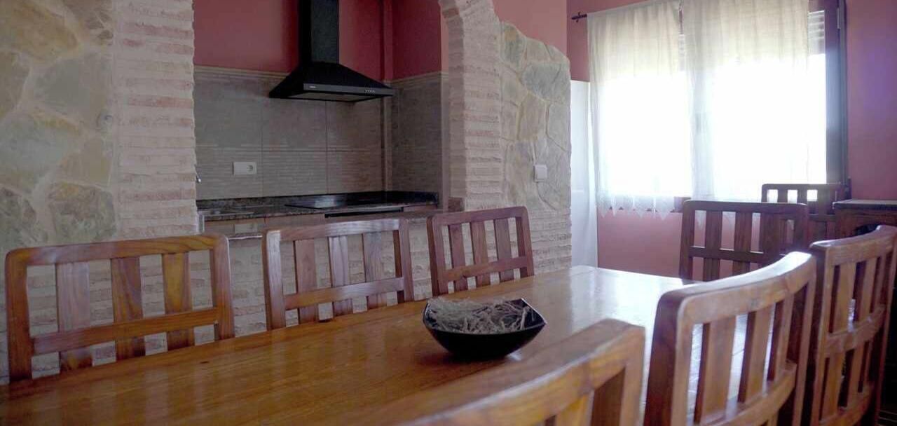 A dining area with a stone wall, a black range hood, and wooden chairs.