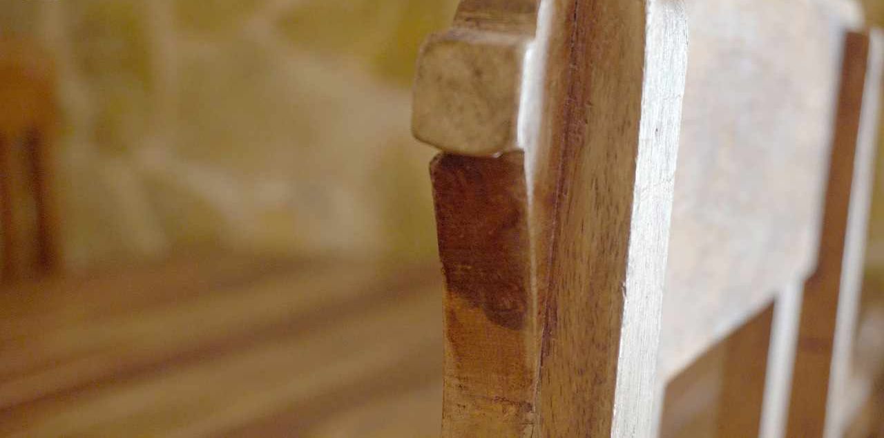 Primer plano de una silla de madera con asiento y respaldo desgastados, evocando un ambiente rústico o tradicional.