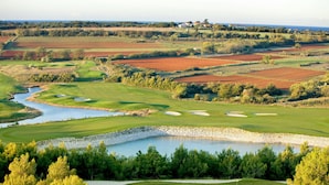Un campo de golf con un estanque, búnkeres de arena y vistas del paisaje circundante.