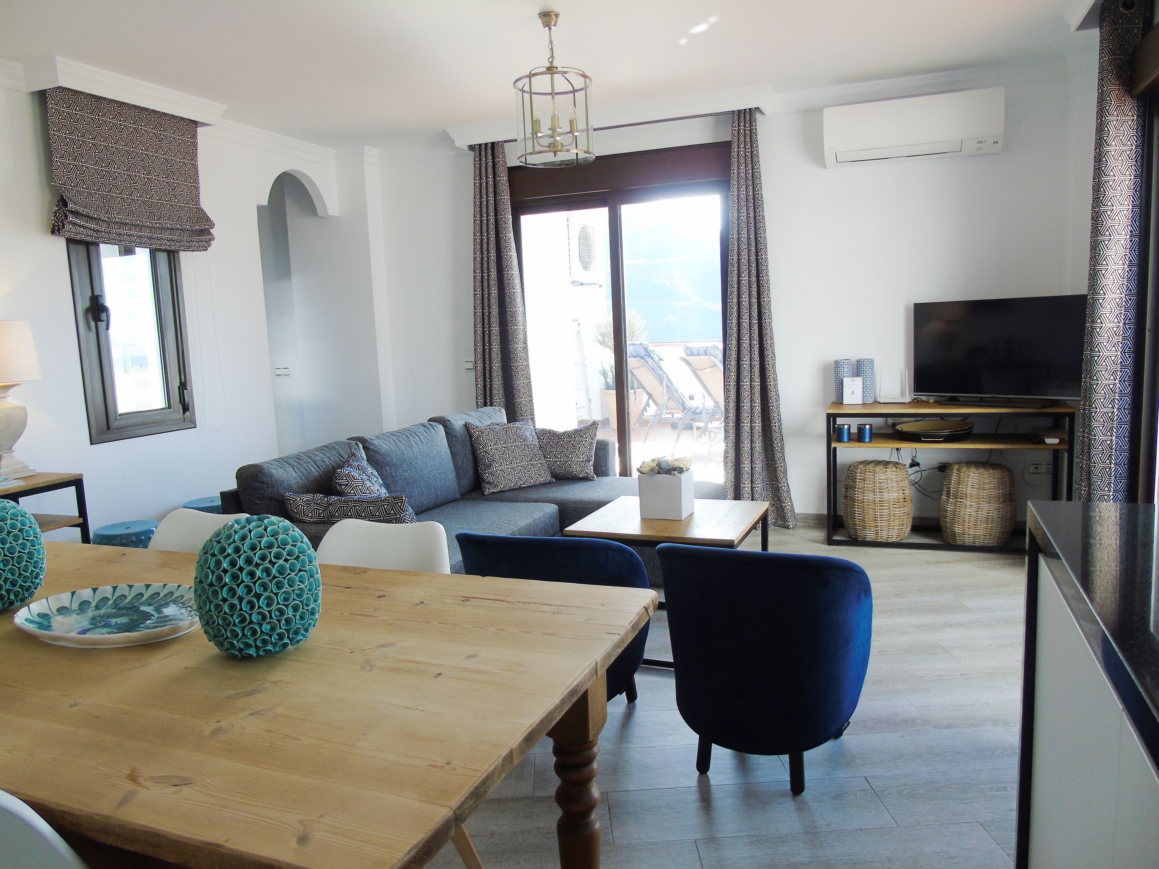 En moderne stue med sofa, stole, et træbord, et fjernsyn og en balkon med udsigt.