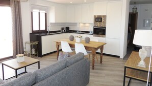 Eine moderne Küche mit weißen Schränken, einem Holzes Esstisch und einem grauen Sofa.