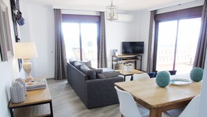Ein modernes Wohnzimmer mit einer Couch, einem Esstisch mit Stühlen, einem Fernseher und Balkonblick.
