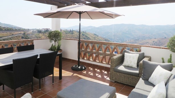 Eine Terrasse mit Tisch, Stühlen und einer Sitzecke, mit Blick auf eine Berglandschaft.
