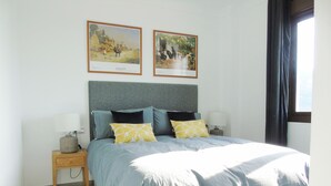 Ein Schlafzimmer mit einem Bett, zwei Nachttischen, einem Kopfteil und zwei gerahmten Bildern an der Wand.