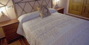 A bed with a patterned bedspread, a decorative pillow, bedside lamps, and a wooden nightstand with a drawer.