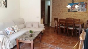 Uma sala de estar com sofá, uma mesa de centro com uma planta, e um espaço de jantar com cadeiras de madeira e uma mesa.