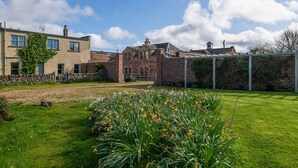 A residential area with a grassy lawn, a garden with daffodils, and a brick house with a stone wall. - A spacious and comfortable cottage (Greenlaw)