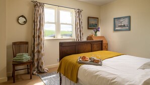 A bedroom with a bed, a chair with a towel, a window with curtains, a dresser, and a tray with breakfast items. - A spacious and comfortable cottage (Greenlaw)