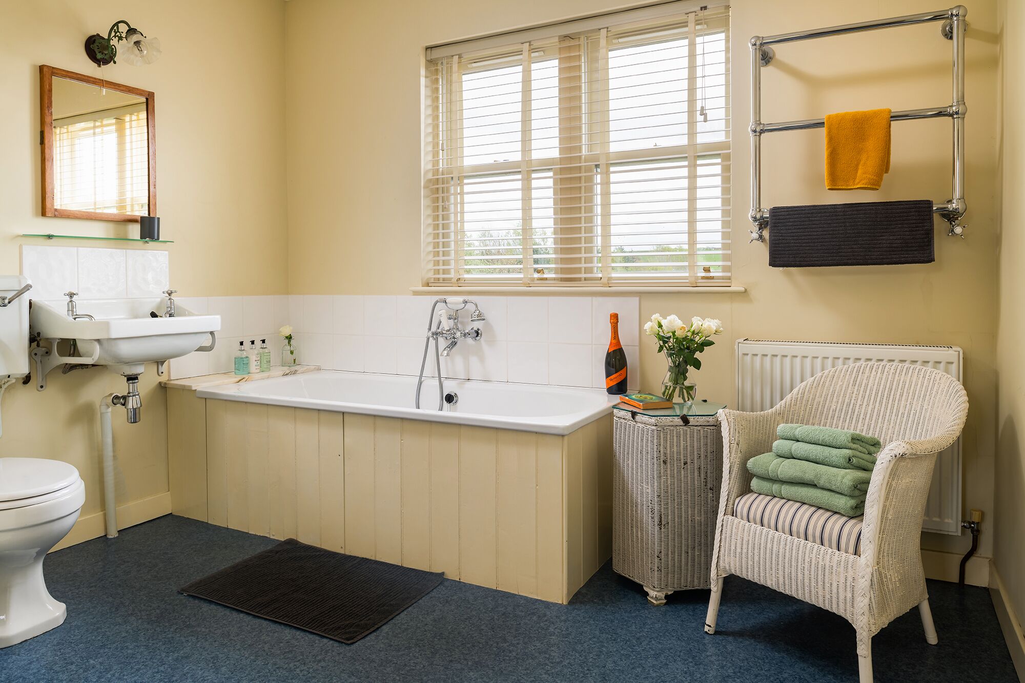 A bathroom with a bathtub, a toilet, a sink, and a wicker chair.