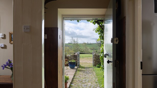 An open door leading to a stone pathway with a view of a rural landscape. - A spacious and comfortable cottage (Greenlaw)