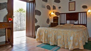 Ein Schlafzimmer mit Bett, Nachttisch, Kommode, einer Tür, die nach draußen führt, und einer Wand mit Steinmuster.