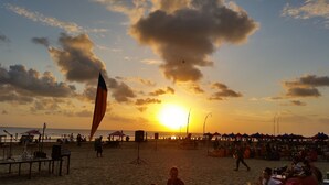 Escena de playa con gente, sombrillas y una bandera.