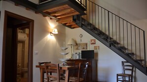 Ein Essbereich mit einem Holztisch und -stühlen, eine Treppe mit Metallgeländer und einer Wandlampe.