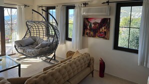 A living room with a hanging chair, a sofa, and a painting on the wall. - 2 bedroom self contained furnished flat with pool, 5 mins walk to town & beach. (Kalkan)