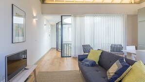 A modern living room with a flat-screen TV, a sofa with cushions, a coffee table, and a dining area with a white table and chairs. - Yellow House - The Skylight (Porto)