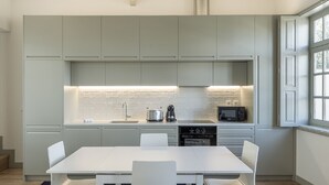 A modern kitchen with white cabinets, a central island, and a dining area with a white table and chairs. - Yellow House - The Skylight (Porto)