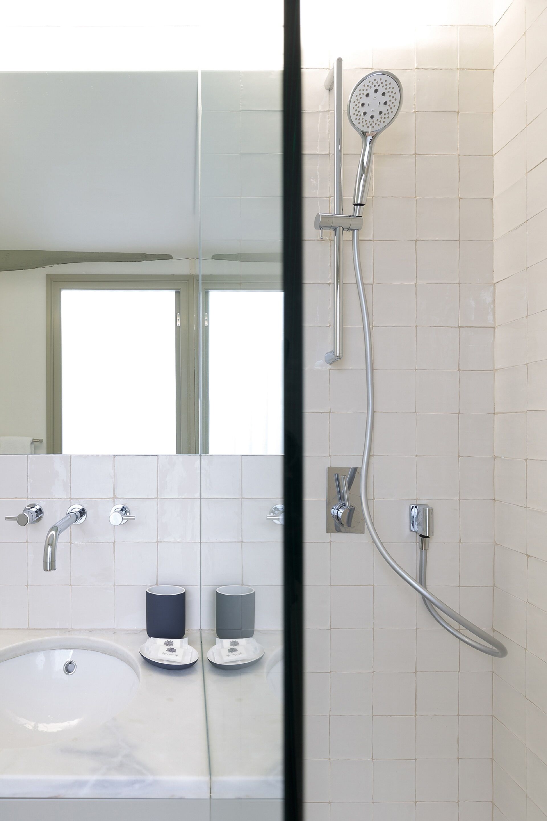 A modern bathroom with a large sink, two soap dispensers, a handheld showerhead, and a mirror.